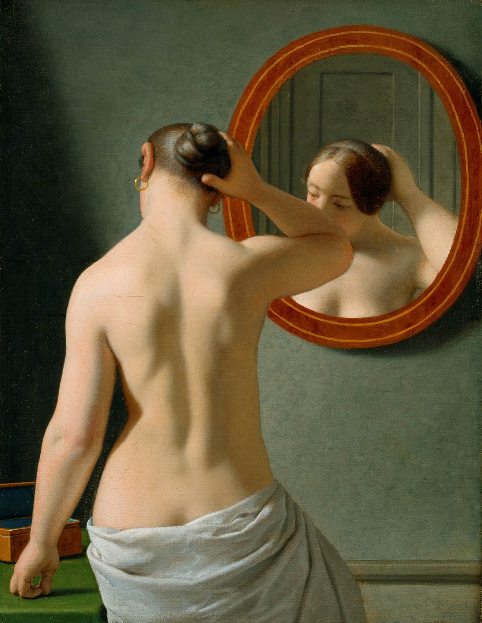 A nude woman doing her hair before a mirror