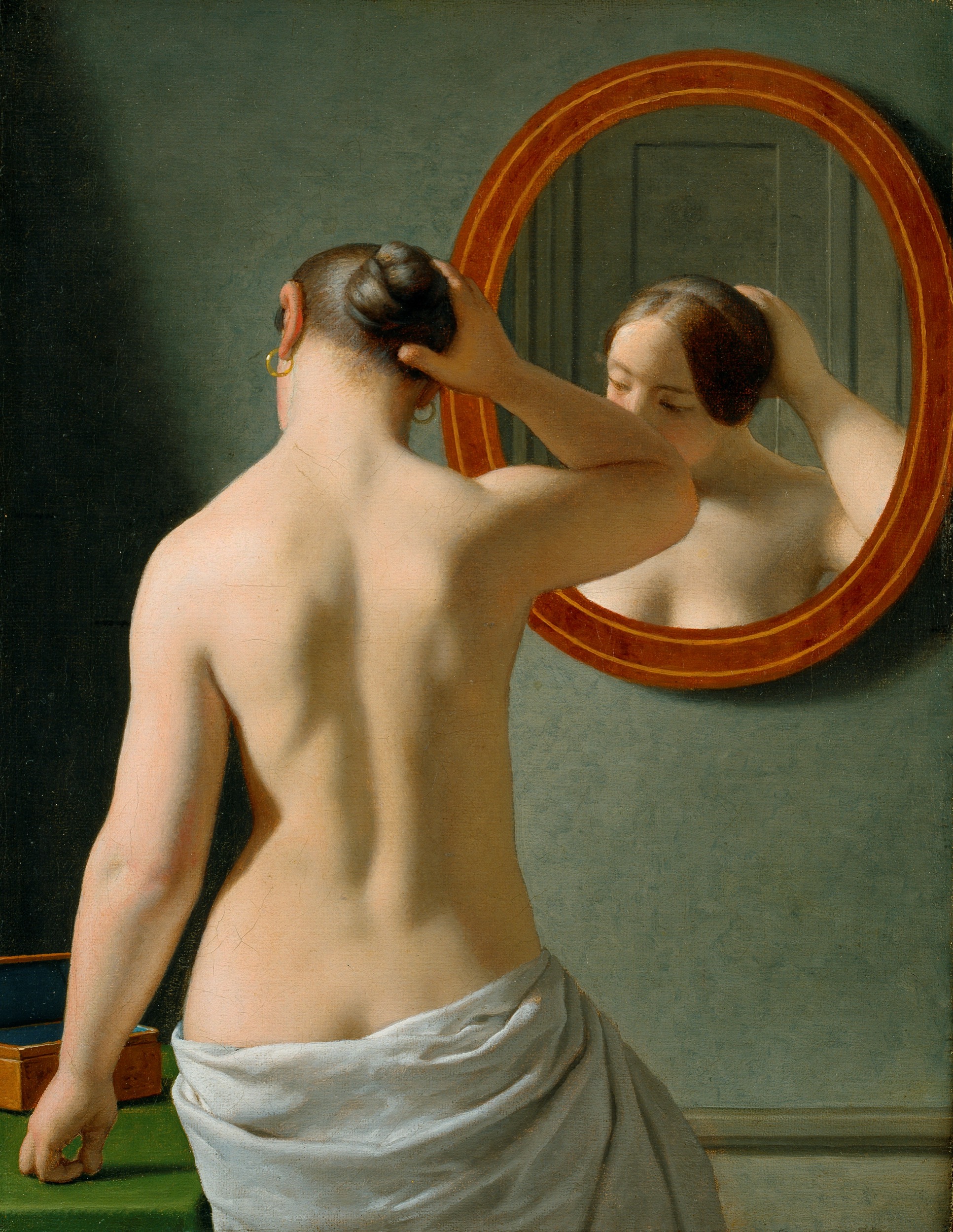 A nude woman doing her hair before a mirror